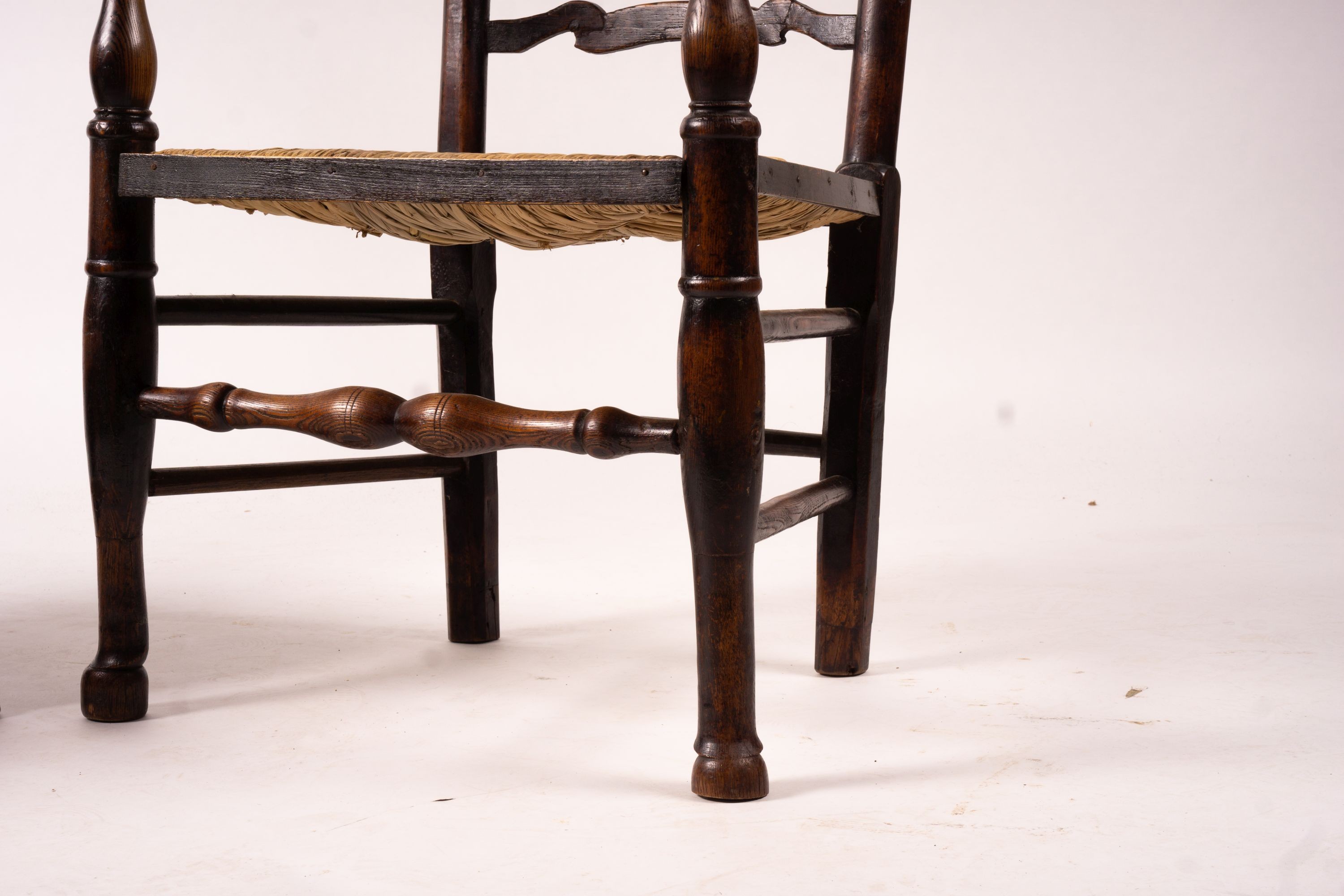 A pair of early 19th century Lancashire ash and fruitwood rush seat ladderback elbow chairs, width 60cm, depth 46cm, height 110cm